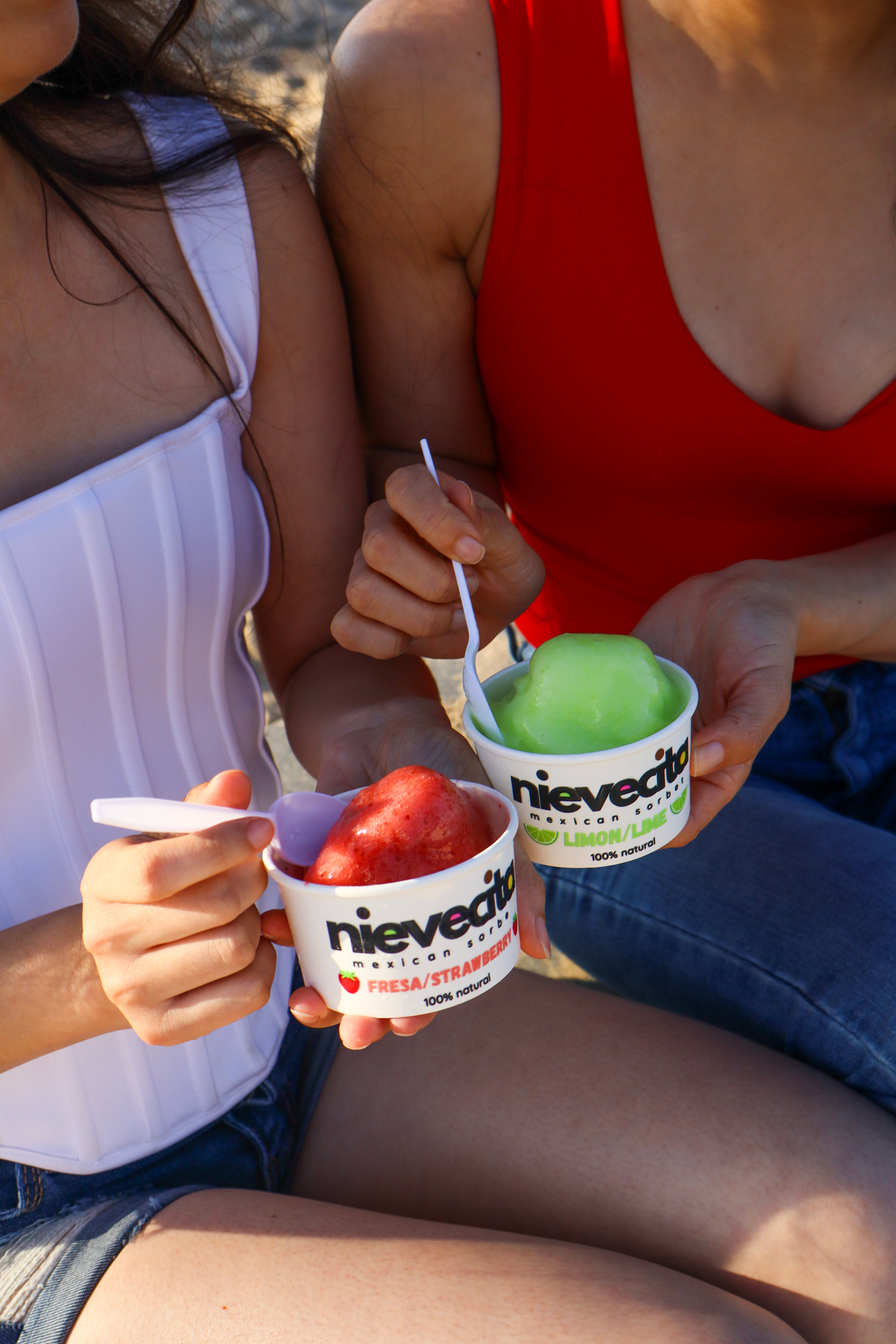 Two people enjoying ice cream sorbet from nievecita in a casual outdoor - beach setting.