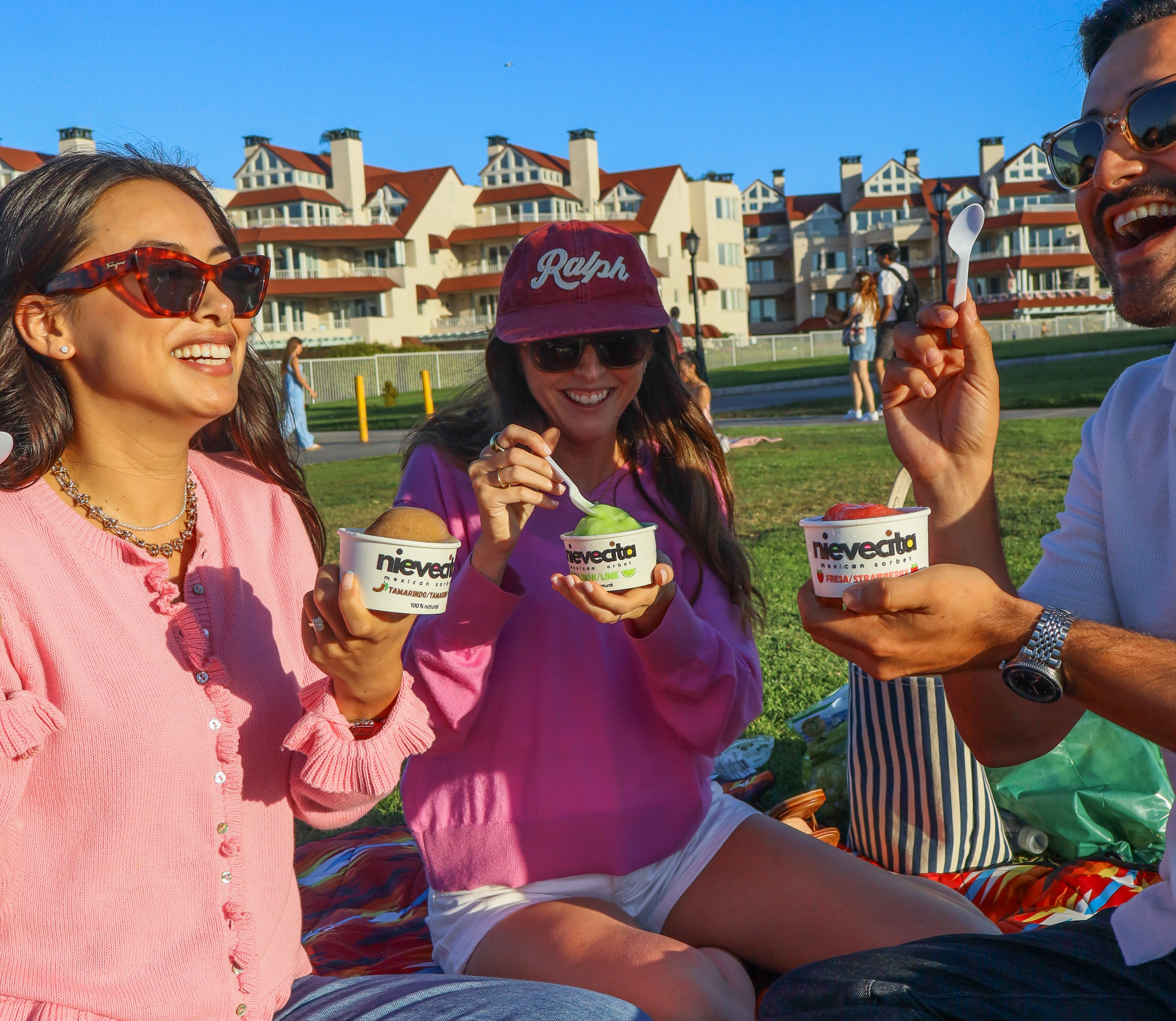 Three people enjoying sorbet ice cream in a park with buildings in the background. Coronado Island , San Diego